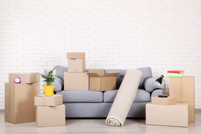 Cardboard boxes with household stuff and grey sofa on brick wall background
